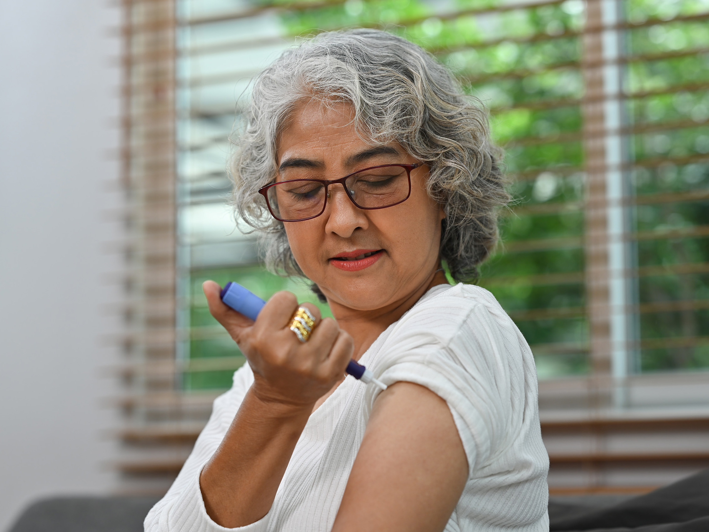 Portrait of a Diabetic mature woman taking an insulin shot on her arm. Diabetes and elderly health care concept